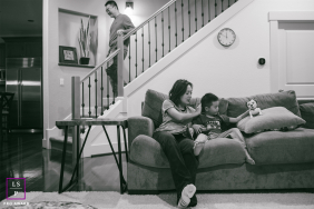 Everyday Family Life Unfolds Quietly With Candid Warmth In Black And White Portrait In Oregon Home In this Oregon home, everyday family life unfolds quietly as a mother reads with her son while the father descends the stairs after bedtime duties. The black and white tones give the candid scene warmth, stillness, and honesty.