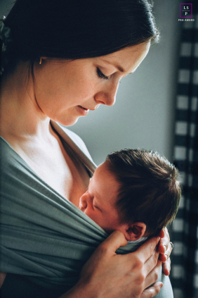 Mother Holds Newborn Close In Tender Protective Burnstown, Ontario Portrait With Warmth And Light In Burnstown, a mother holds her newborn close against her chest with quiet protectiveness and calm focus. The soft directional light and intimate framing give the photograph warmth, tenderness, and the deep comfort of early connection.