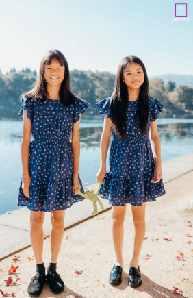 Mirroring Twins Stand Together Beside Water in Warm Fall Sunlight in San Ramon, California In San Ramon, California, the twins stand together in the warm fall sunlight beside the water, nearly mirroring one another in pose and expression. The soft light and matching dresses give the portrait sweetness, balance, and quiet sibling connection.