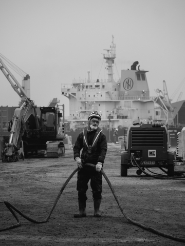 Um trabalhador habilidoso da construção civil de Charente Maritime, usando capacete, segura uma linha de energia com determinação. Esta imagem poderosa captura a expertise e o profissionalismo da Spie Batignolles Fondations.