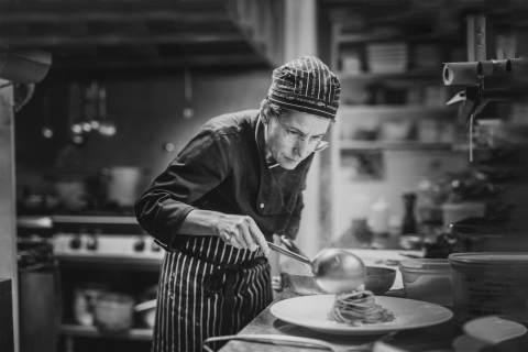 Retrato em preto e branco da Chef Nicoletta na cozinha do Ristorante il Mestolo, em Siena, Toscana, Itália. Capturando seu foco e paixão enquanto trabalha, esta imagem destaca a arte do artesanato culinário.