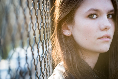 An Auvergne-Rhone-Alpes Close up portrait of a teenage girl against a fence during a lifestyle shoot in Savoie