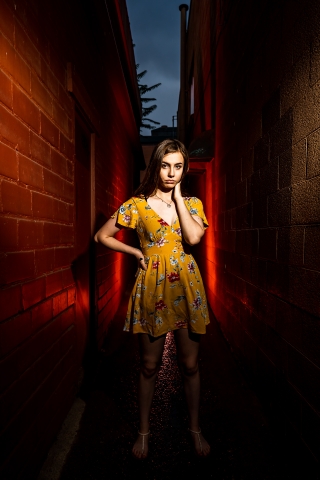 A Colorado High school senior poses in an alley lit with red during a late afternoon lifestyle photo session in Boulder