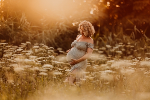 This is a lifestyle image from Flevoland, Netherlands of a woman in grass field holding belly during maternity pregnancy shoot