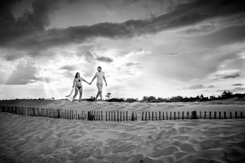 Em Herault Occitanie, o casal caminha na duna de areia durante uma sessão de maternidade BW