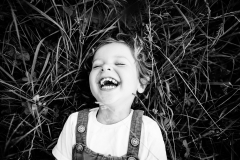 In Marcy l'étoile, France, a captivating black and white overhead shot captures a smiling boy, utterly content, resting in the midst of lush grass