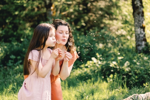 Um retrato de estilo de vida mostra mãe e filha em Redmond, WA, aproveitando a primavera juntas soprando narcisos
