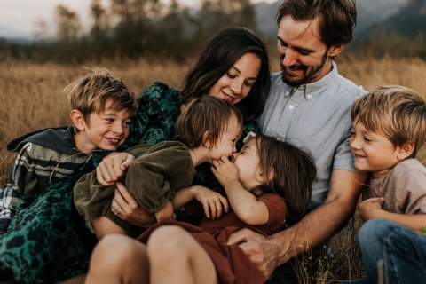 This heartwarming lifestyle portrait captures a big family cuddling happily in a picturesque dry grass field in beautiful Oregon. Mom, dad, and their four adorable kids radiate joy and togetherness.