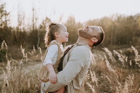 The lifestyle portrait captures the joyous bond between a father and child, as they share laughter in the golden fields of North France