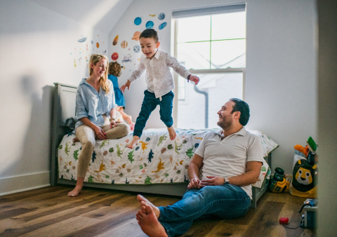 In Dallas, Texas, a family picture shows a boy joyfully jumping off his bed with his parents smiling and watching at their home.