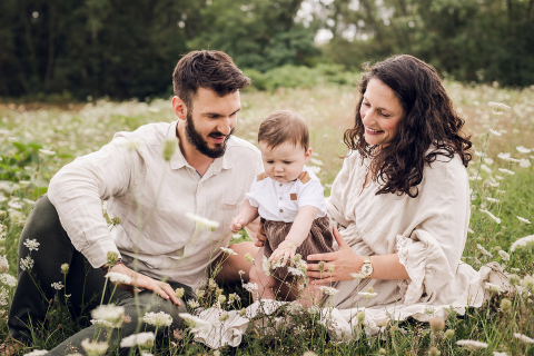 Uma imagem de estilo de vida criada em Lyon, França: um retrato de família em um campo florido onde pai, mãe e filho estão sentados felizes entre flores coloridas.