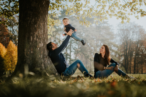 A photo taken in Paris shows a young boy having fun with his parents at the park, playing happily under a shady tree.