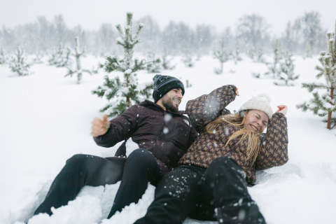 Numa cena acolhedora em Lofoten, na Noruega, um casal senta-se na neve, atirando neve de forma divertida e rindo no meio de pinheiros imponentes.