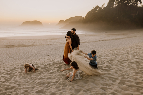 Uma imagem de estilo de vida criada em Cannon Beach, Oregon, mostrando uma família brincando alegremente e jogando areia na praia.