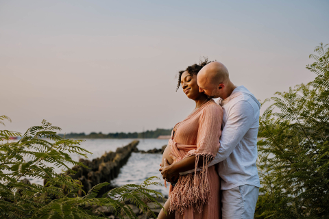 Em um rio em Portland, Oregon, a foto de um homem abraçando sua esposa grávida, capturando o amor e a expectativa de sua crescente família em um ambiente tranquilo ao ar livre.