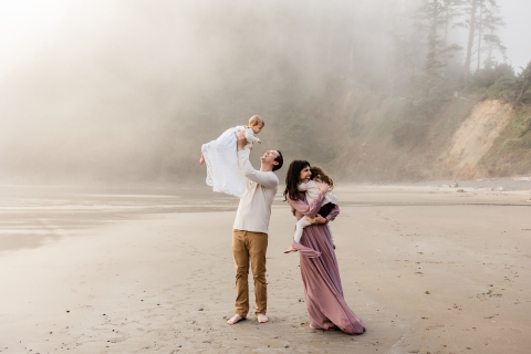 A foto de uma família com um bebê e uma menina na praia no noroeste do Pacífico ao pôr do sol em uma noite de neblina.