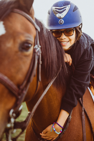 In Miami, a girl posed with her first horse, wearing riding gear, as she leaned forward in the saddle with a big smile while hugging the horse.