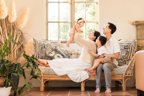 Uma família feliz de quatro pessoas em sua casa em Ventura, Califórnia, sentada alegremente em um sofá de vime perto de uma janela, aproveitando o tempo juntos.