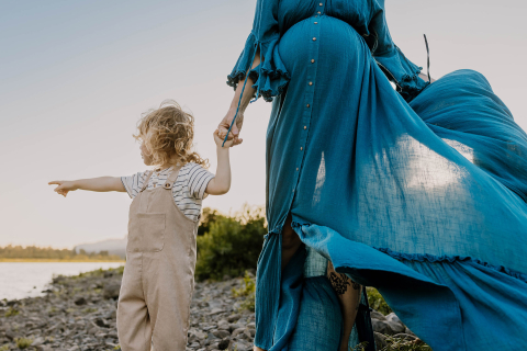 Em Cascade Locks, Oregon, uma mãe grávida em um vestido azul esvoaçante segura gentilmente a mão de seu filho pequeno enquanto eles estão em meio ao cenário cênico