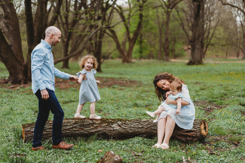 Família aproveitando uma caminhada na natureza na floresta, usando uma árvore caída como banco e trave de equilíbrio para sua filha pequena em Boston, Massachusetts.