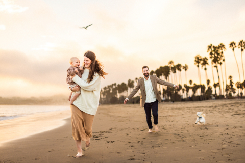Família de três pessoas e seu cachorro sorrindo na praia de Santa Bárbara, cercados de amor e felicidade.