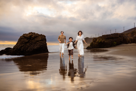 Uma família de três pessoas correndo alegremente pela praia chuvosa em Los Angeles, Califórnia, EUA, capturada em um pitoresco retrato de estilo de vida.