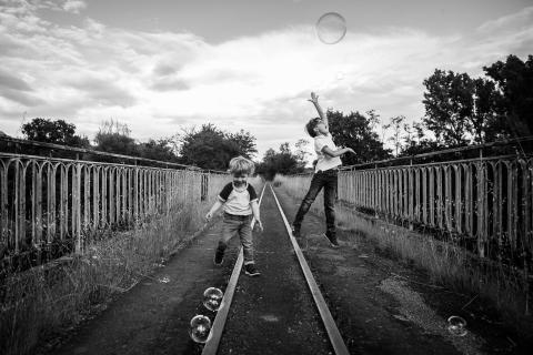 Dois meninos correm alegremente atrás de bolhas nos trilhos do trem na pitoresca zona rural de Haute-Garonne.