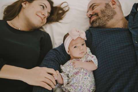 Um retrato de estilo de vida emocionante, mostrando um casal apaixonado em Nova Jersey se olhando enquanto se aconchegam com sua preciosa filha recém-nascida em uma cama aconchegante.