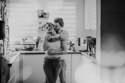 Em Oppenheim, Renânia-Palatinado, Alemanha, uma foto em preto e branco captura um casal se abraçando na cozinha. A cena íntima destaca o calor e o afeto em um ambiente aconchegante e cotidiano.
