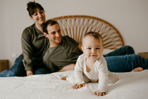 Na Provença, um retrato de família na cama mostra uma menina sorridente em primeiro plano, com seus pais também sorrindo suavemente ao fundo.