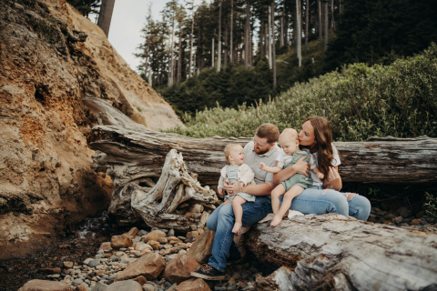 Na Costa do Oregon, EUA, pais aproveitam um dia de praia com seus filhos gêmeos sentados em um tronco.