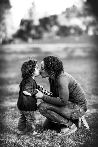 Em Mountain View, Califórnia, um retrato vertical de família em preto e branco captura uma mãe beijando carinhosamente seu filho pequeno no parque.