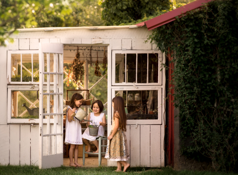 Três irmãs riem em pé na porta de uma estufa em Chattanooga, Tennessee. A cena lembra uma pintura de Norman Rockwell.