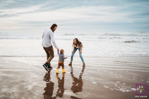 Uma família cheia de alegria de três pessoas, capturada em um delicioso retrato de estilo de vida, deleitando-se com risadas e aventuras em Cannon Beach, Oregon, durante a maré baixa