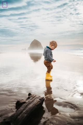 Uma criança adorável com curiosidade sem limites vagueia pelas areias encantadoras de Cannon Beach, Oregon, durante a maré baixa, calçando preciosas botinhas amarelas