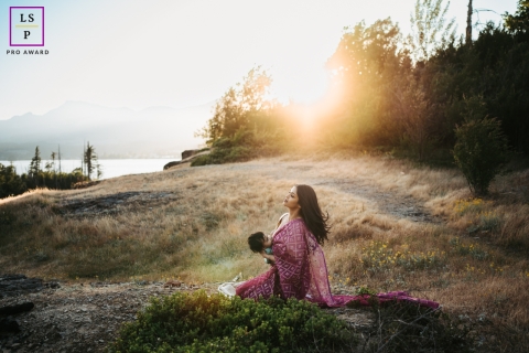 In the scenic Cascade Locks of Oregon, a serene field near water provides the backdrop as a stunning mother effortlessly nourishes her son through breastfeeding, capturing the essence of a peaceful and cherished lifestyle portrait