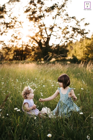 Em um campo sereno de Camas, Washington, duas irmãs encontram alegria em brincar com flores silvestres, uma cena perfeita para um retrato de estilo de vida