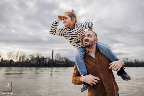 Em Lyon, França, um pai carrega a filha nos ombros enquanto ela se inclina para a frente, protegendo os olhos com a mão, e olha para o longe.