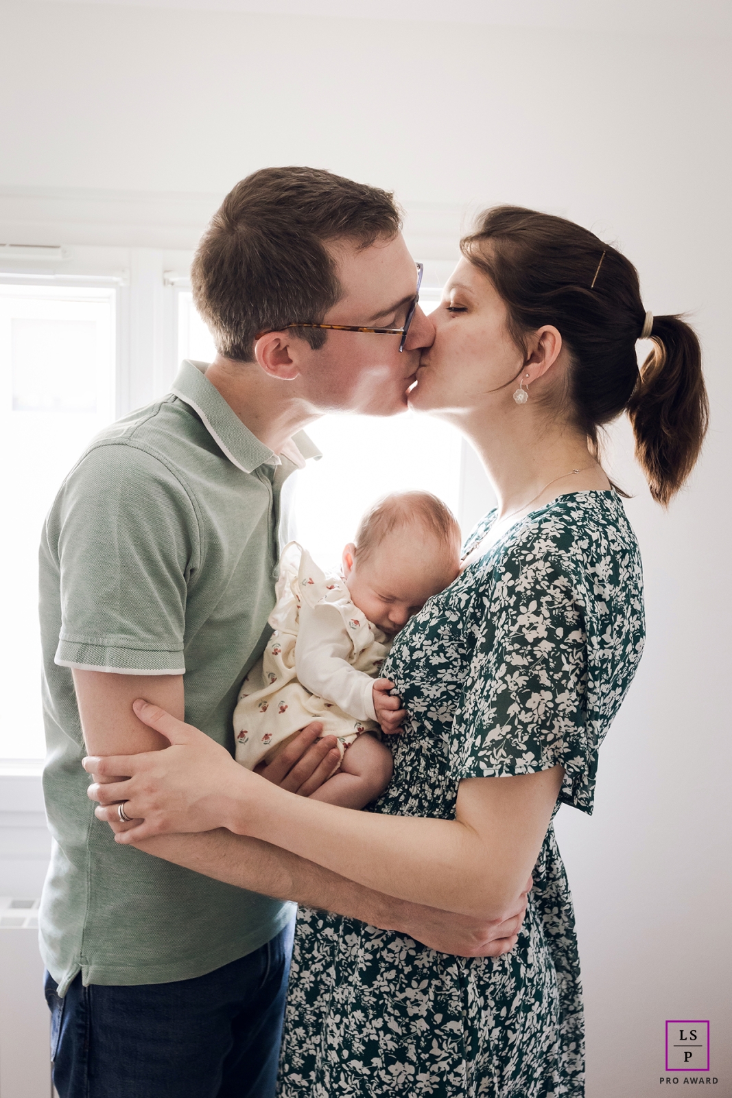 This intimate lifestyle portrait captures a heartwarming young family in Lyon, France, as they cuddle their precious baby and share a tender kiss.