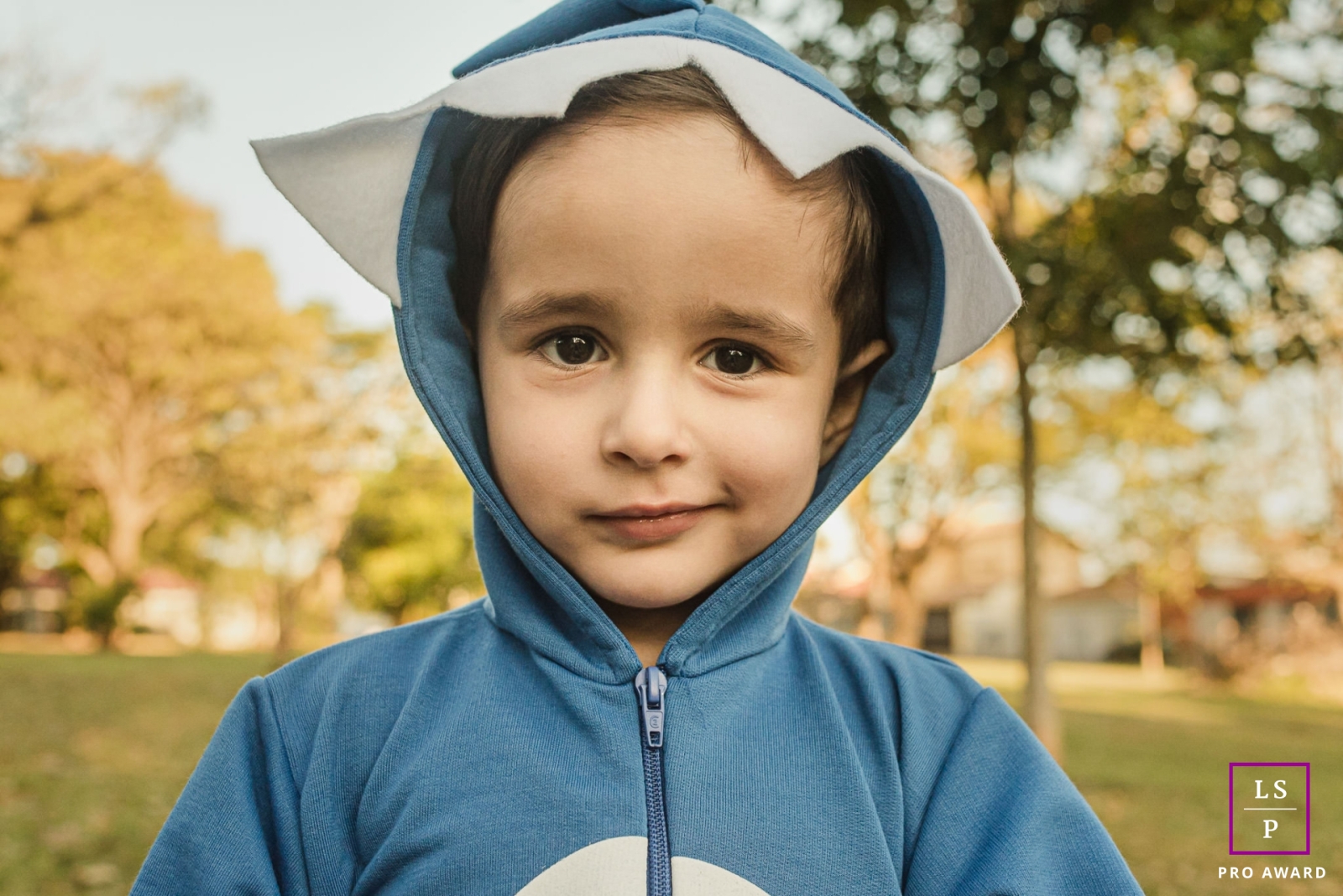 A mischievous smirking kid dressed in a shark costume, poses for a portrait during a lively lifestyle photo session in Campo Grande, Brazil.