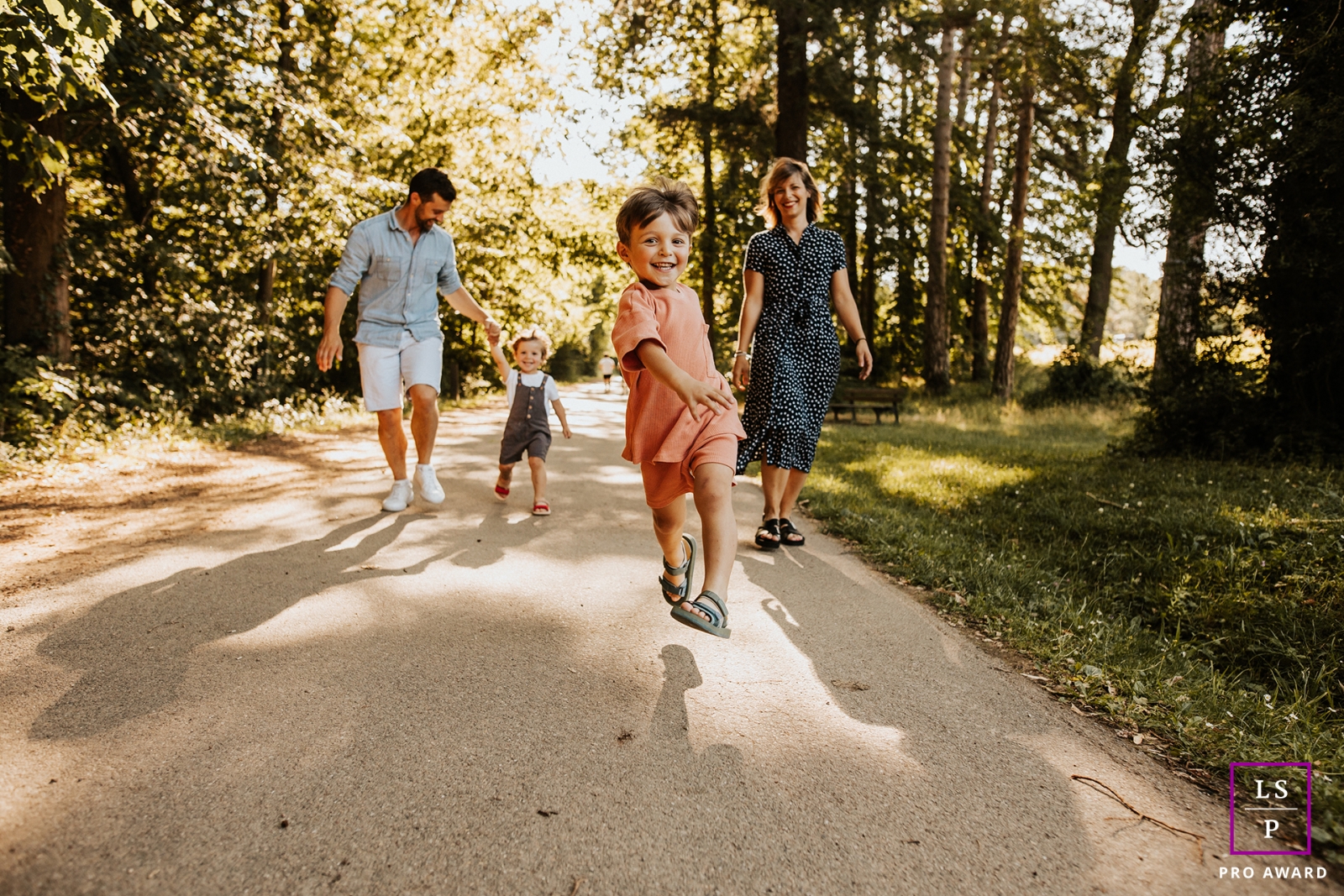 Uma família de 4 pessoas em Marcy l'étoile, França, corre e salta alegremente por um caminho pitoresco arborizado durante uma sessão de retratos de estilo de vida