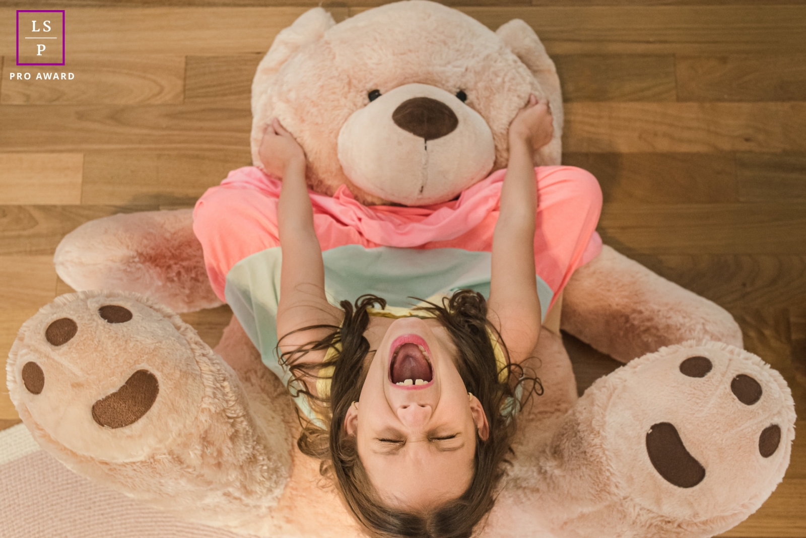 This happy girl is screaming and laughing with her giant stuffed bear at Campo Grande, Brazil in this stunning lifestyle portrait shot from above