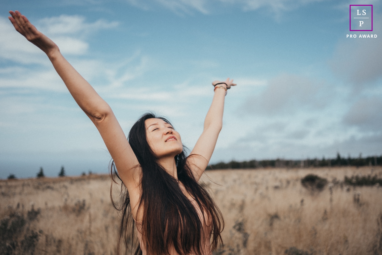 In this stunning portrait in Nova Scotia, a woman stands in a field of weeds with arms outstretched, exalting in the beauty of the vibrant blue sky above her