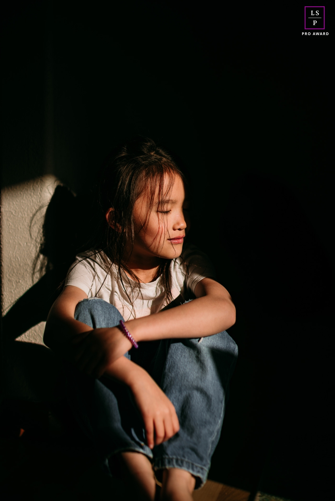 At home in Denver, Colorado, this young woman is peacefully nestled in a cozy atmosphere, enveloped in both light and darkness