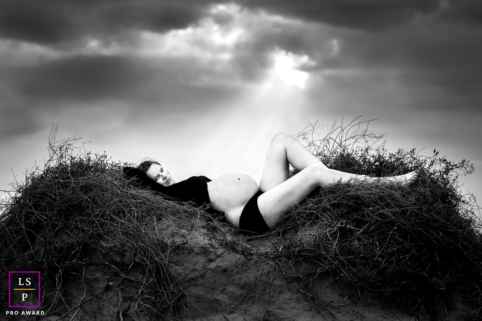 In the Hérault region of France, this black and white image captures a beautiful pregnant woman, cozily nestled beneath the clouds