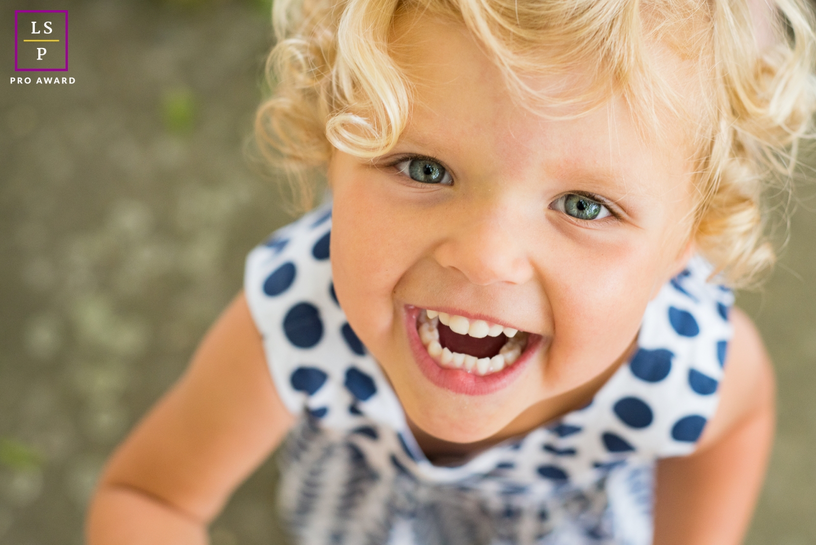 In France, Provence, a little blonde girl with cute teeth on display and cute curls of hair behind her is smiling at the camera.In France, Provence, a little blonde girl with cute teeth on display with cute curls of hair is smiling at the camera