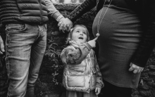 The child’s wide-eyed wonder provides a delightful centerpiece as she points toward the mystery of her mother’s pregnant belly. This black and white frame masterfully captures a beautiful, curious family threshold.