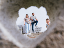 Framed through a heart shaped opening in Bardos, this family appears surrounded by humor, love, and unfinished construction. The playful perspective and unexpected peeking child give the photograph charm, creativity, and lighthearted storytelling.