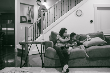 In this Oregon home, everyday family life unfolds quietly as a mother reads with her son while the father descends the stairs after bedtime duties. The black and white tones give the candid scene warmth, stillness, and honesty.