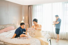 In this Chengdu home, excitement quietly fills the room as the family gathers around clothes prepared for the new baby. The soft window light and layered arrangement of each family member give the photograph warmth, anticipation, and gentle everyday joy.